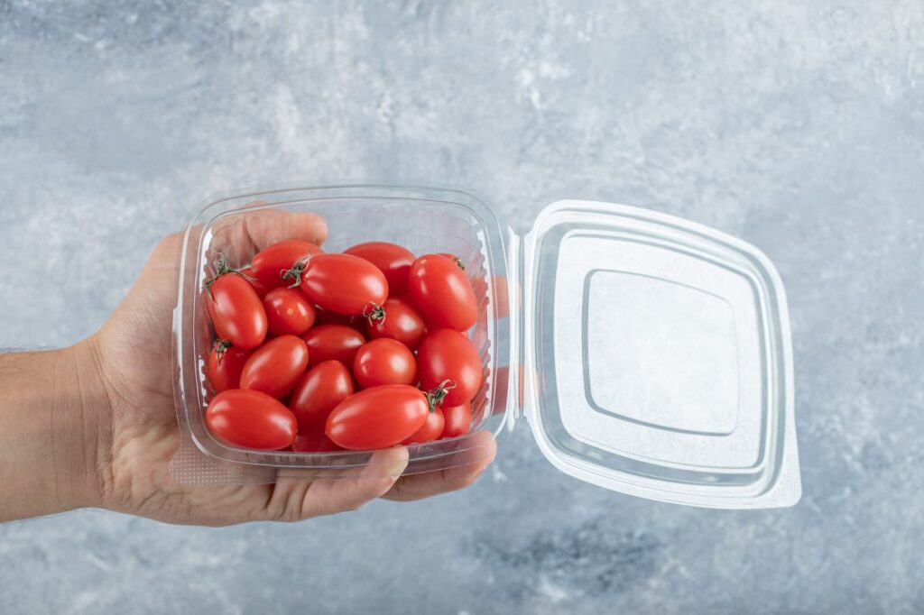 Man holding small red cherry tomatoes in a plastic container