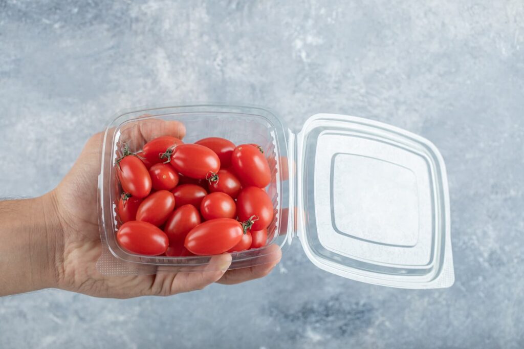 Man holding small red cherry tomatoes in a plastic container